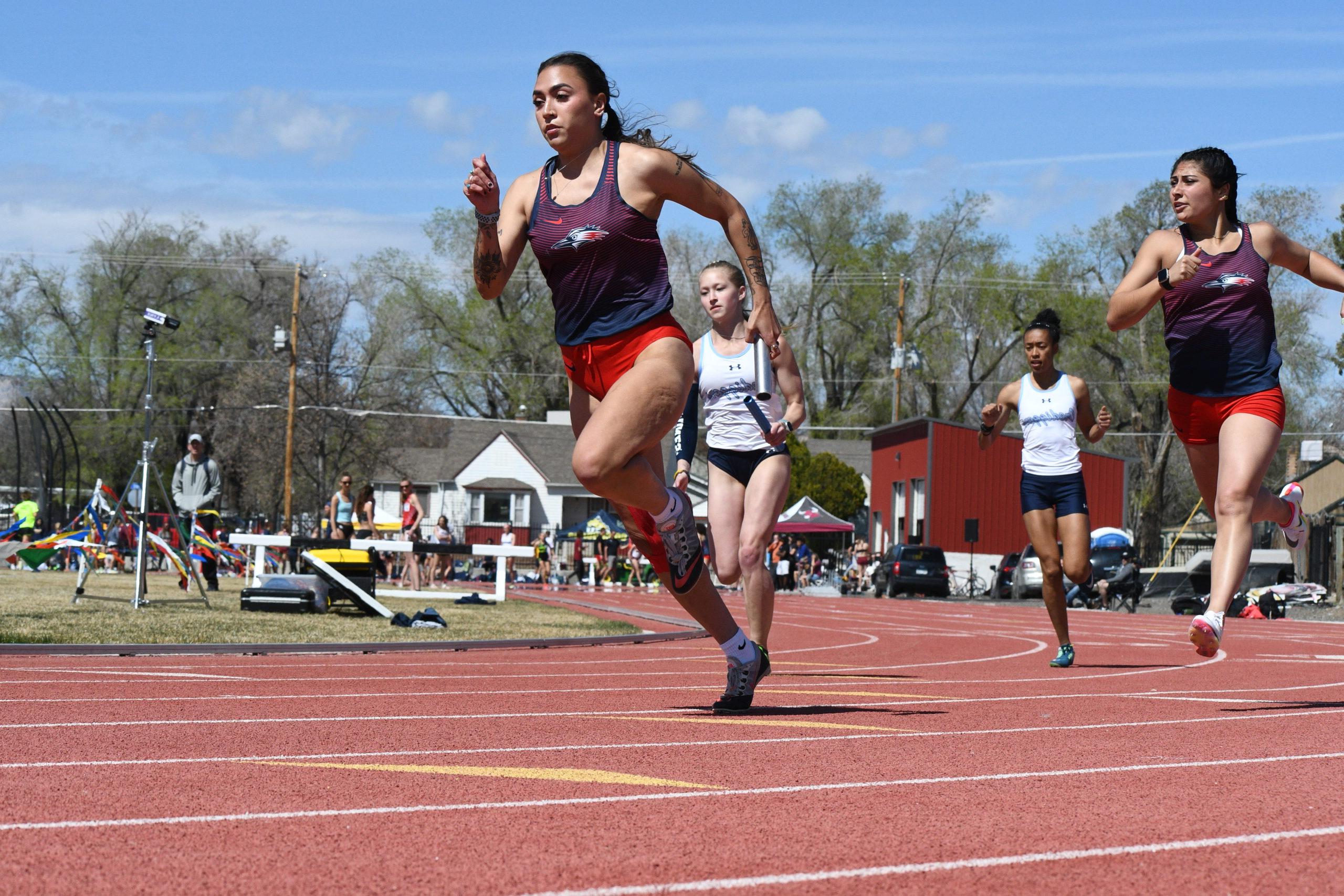 Women's track athlete Allyssa Romero leads during a relay race after receiving a handoff.